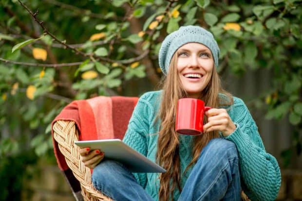 Junge Frau mit Mütze sitzt draußen in der Natur mit einer Tasse Mate Tee