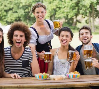 Gruppe junger Menschen sitzen an einem Holztisch und trinken Bier auf dem Oktoberfest
