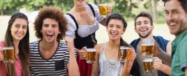 Gruppe junger Menschen sitzen an einem Holztisch und trinken Bier auf dem Oktoberfest