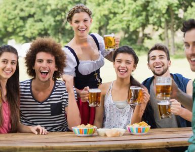 Gruppe junger Menschen sitzen an einem Holztisch und trinken Bier auf dem Oktoberfest