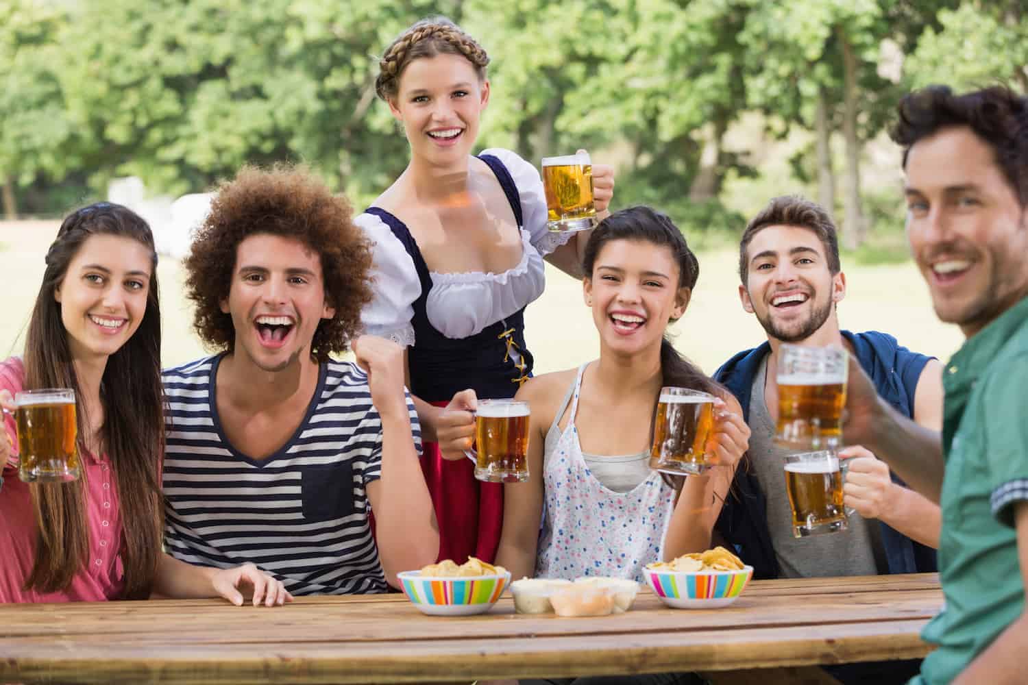 Gruppe junger Menschen sitzen an einem Holztisch und trinken Bier auf dem Oktoberfest