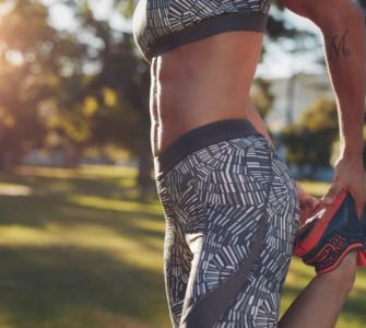 Frau draußen im Park mit Sixpack von der Seite hält einen Fuß und dehnt sich