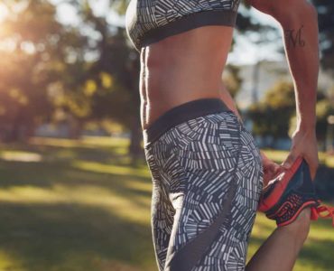 Frau draußen im Park mit Sixpack von der Seite hält einen Fuß und dehnt sich