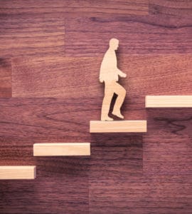 Holzhintergrund davor Männchen dass die Treppe Schritt für Schritt nach oben geht