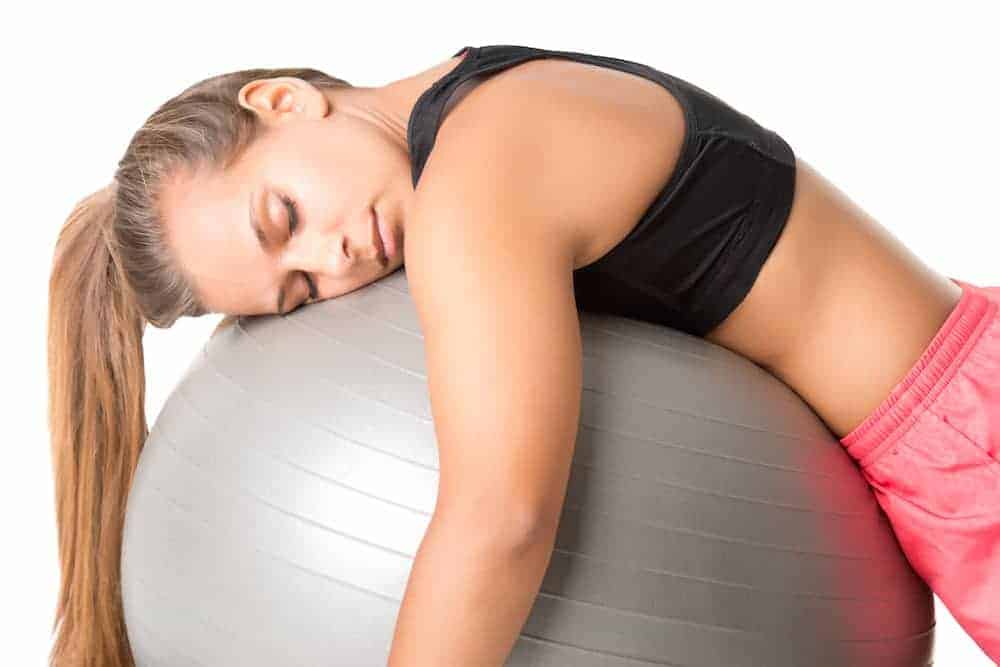 Junge Frau in Sportkleidung schläft beim Training auf einem Pezziball