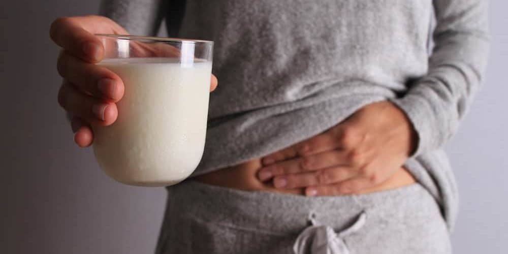 Laktoseintoleranz Frau mit Milchglas in der Hand fasst sich an den Bauch, hat Blähungen durch Laktoseintoleranz