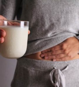 Frau mit Milchglas in der Hand fasst sich an den Bauch, hat Blähungen durch Laktoseintoleranz