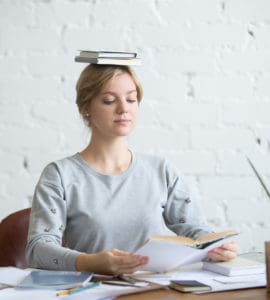 Frau sitzt gerade mit einem Buch auf dem Kopf bei der Arbeit