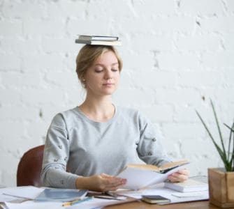Frau sitzt gerade mit einem Buch auf dem Kopf bei der Arbeit