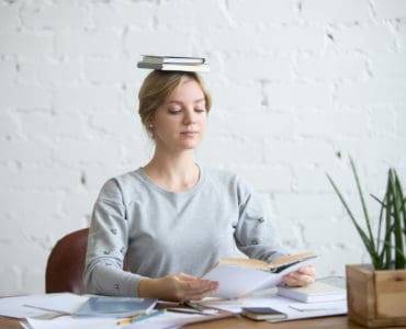 Frau sitzt gerade mit einem Buch auf dem Kopf bei der Arbeit