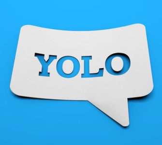 weißes schild mit YOLO in sprechblasenform vor blauem Hintergrund