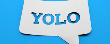 weißes schild mit YOLO in sprechblasenform vor blauem Hintergrund