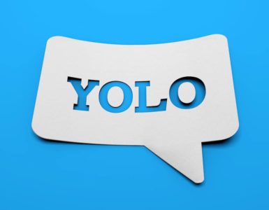 weißes schild mit YOLO in sprechblasenform vor blauem Hintergrund