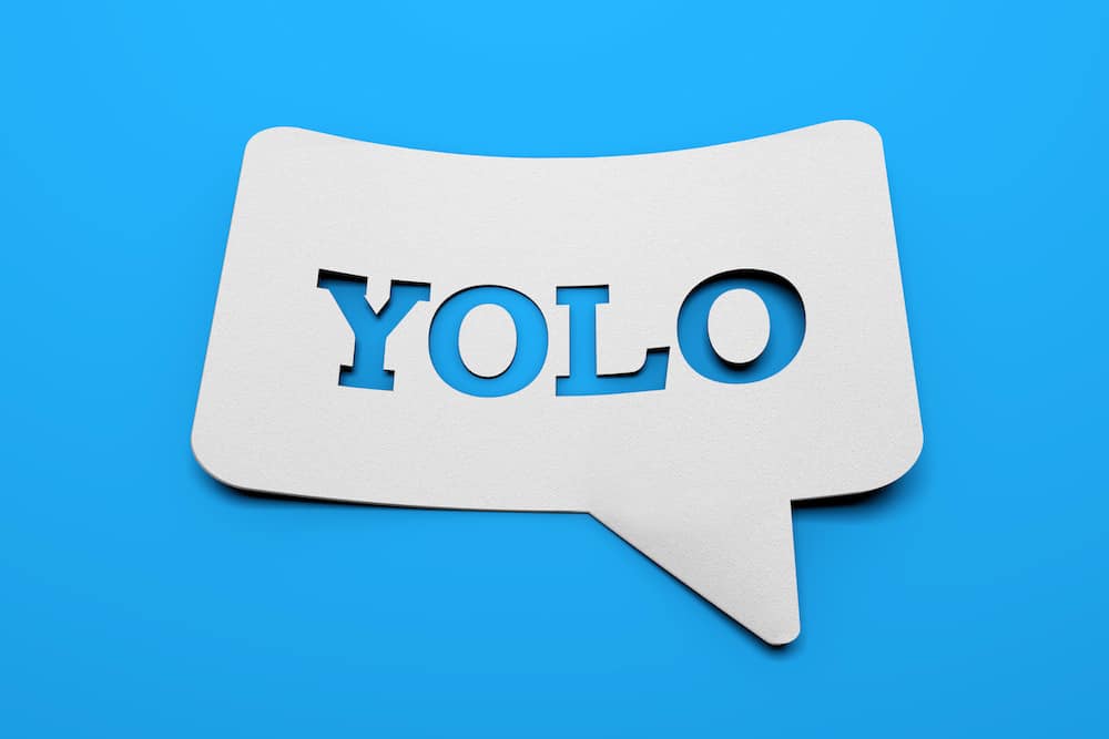 weißes schild mit YOLO in sprechblasenform vor blauem Hintergrund
