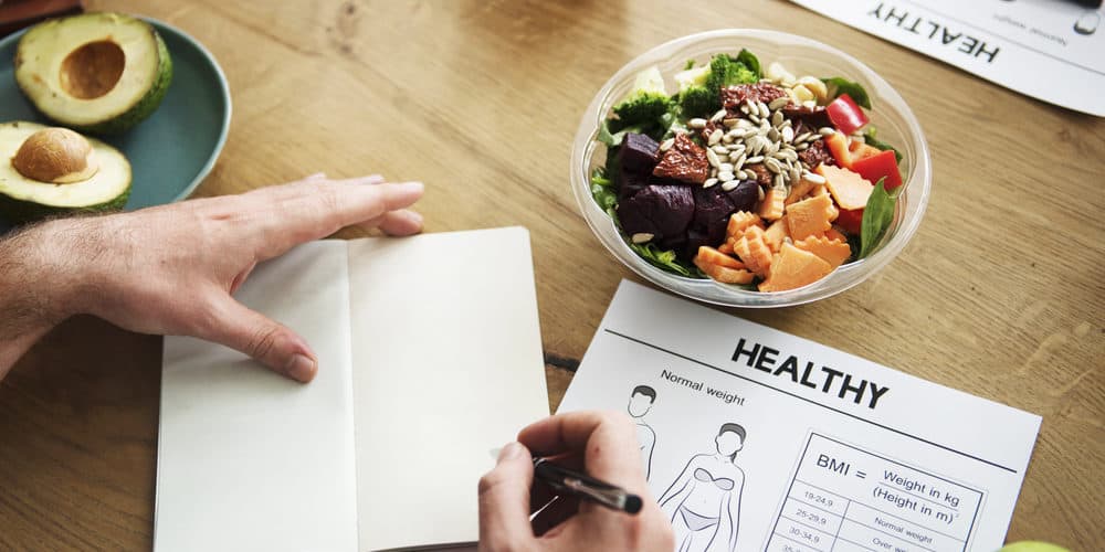 BMI Ein Notizbuch mit Aufzeichnungen zu einer geusnden Ernährung auf einem Tisch mit gesundem Essen