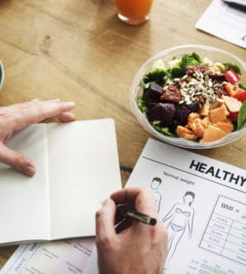 Ein Notizbuch mit Aufzeichnungen zu einer geusnden Ernährung auf einem Tisch mit gesundem Essen