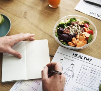Ein Notizbuch mit Aufzeichnungen zu einer geusnden Ernährung auf einem Tisch mit gesundem Essen