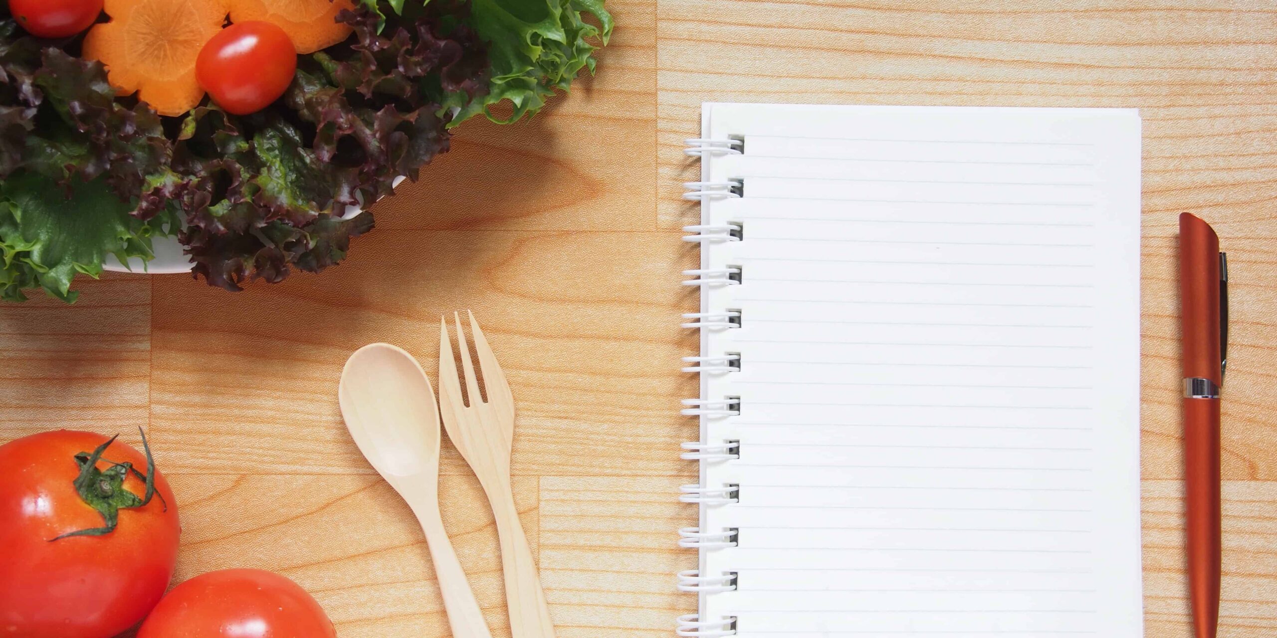 Ernährungsumstellung Tools Holztisch mit gesundem frischem Gemüse und einem unbeschriebenen Ringblock mit Kuli daneben