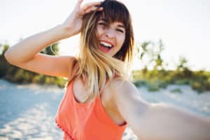 Junge Frau mit orangenem Trägretkleid lacht und ist glücklich
