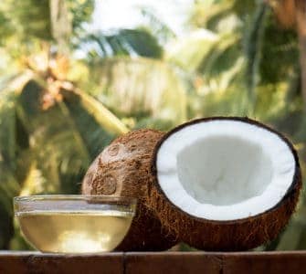 Kokosnusshälfte auf Tisch und Schale aus Glas gefüllt mit Kokosöl