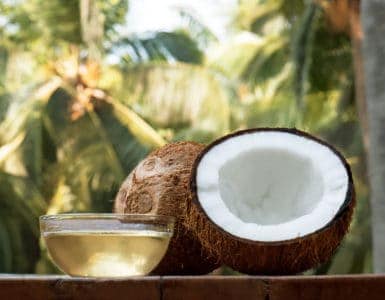 Kokosnusshälfte auf Tisch und Schale aus Glas gefüllt mit Kokosöl