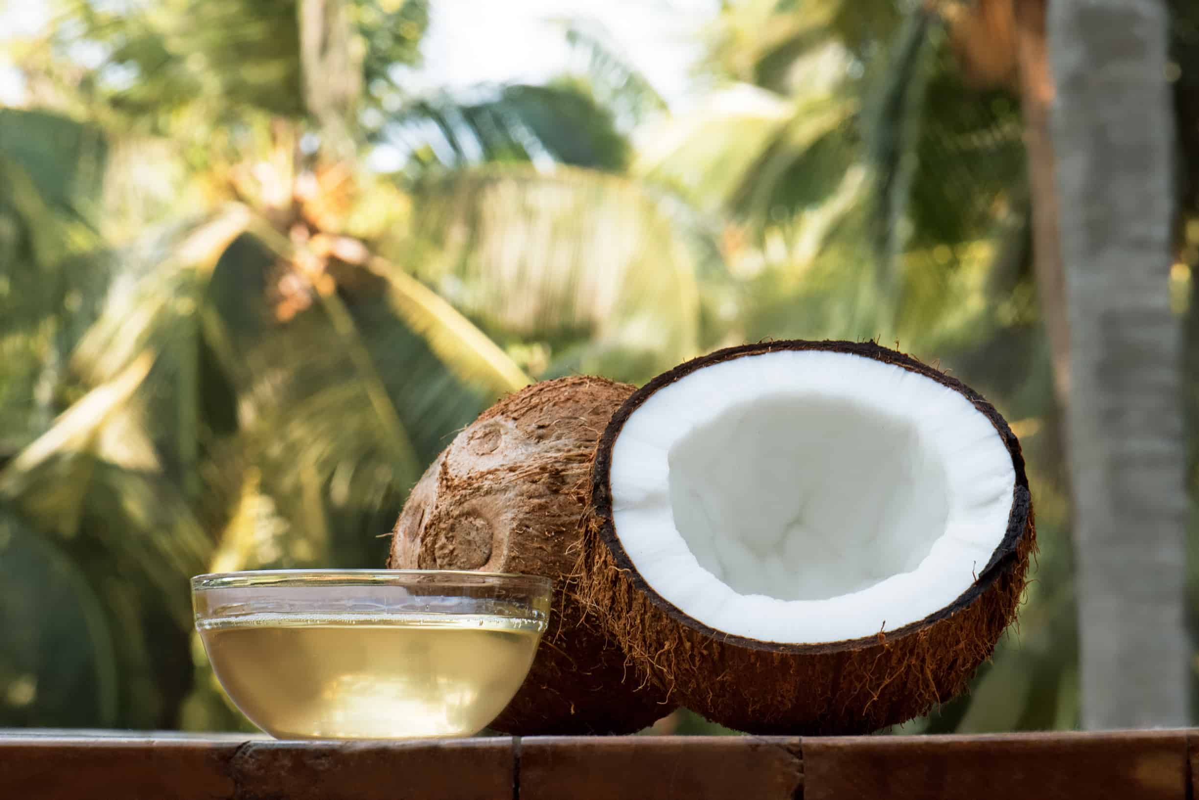 Kokosnusshälfte auf Tisch und Schale aus Glas gefüllt mit Kokosöl