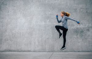 Junge Frau in sportlichem Outfit trainiert vor grauer Steinwand. Sie macht HIIT, den Fitness Trends 2018