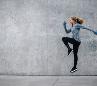 Junge Frau in sportlichem Outfit trainiert vor grauer Steinwand. Sie macht HIIT, den Fitness Trends 2018