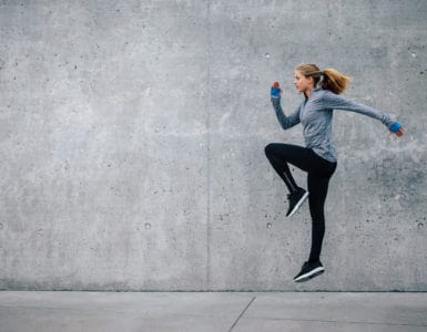 Junge Frau in sportlichem Outfit trainiert vor grauer Steinwand. Sie macht HIIT, den Fitness Trends 2018