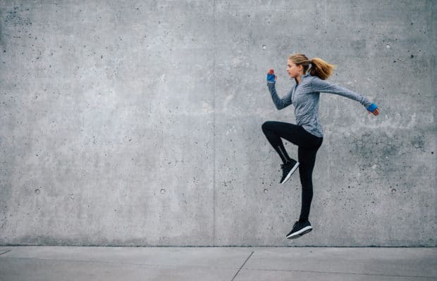 Junge Frau in sportlichem Outfit trainiert vor grauer Steinwand. Sie macht HIIT, den Fitness Trends 2018