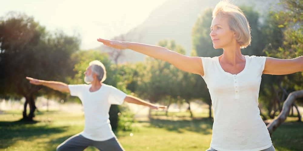 Bewegung ist gesund Eine Frau Mitte 50 und ihr Mann machen im Park Yogaübungen, denn Bewegung ist gesund