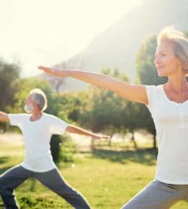Eine Frau Mitte 50 und ihr Mann machen im Park Yogaübungen, denn Bewegung ist gesund