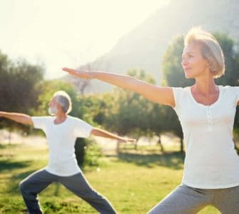 Eine Frau Mitte 50 und ihr Mann machen im Park Yogaübungen, denn Bewegung ist gesund