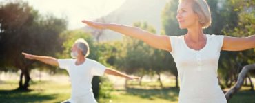 Eine Frau Mitte 50 und ihr Mann machen im Park Yogaübungen, denn Bewegung ist gesund