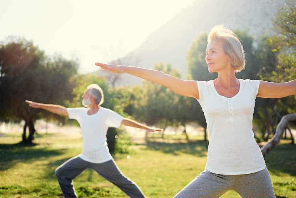 Eine Frau Mitte 50 und ihr Mann machen im Park Yogaübungen, denn Bewegung ist gesund