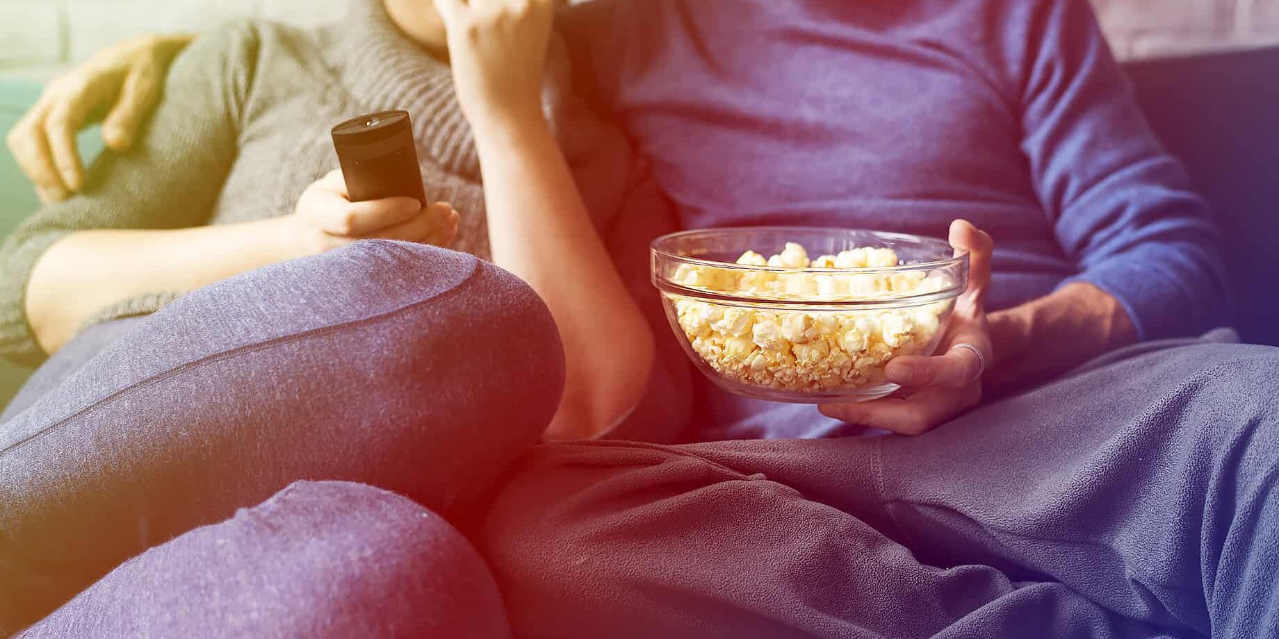 Speck ein Paar sitzt auf dem Sofa und isst poppcorn und trinkt bier