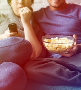 ein Paar sitzt auf dem Sofa und isst poppcorn und trinkt bier