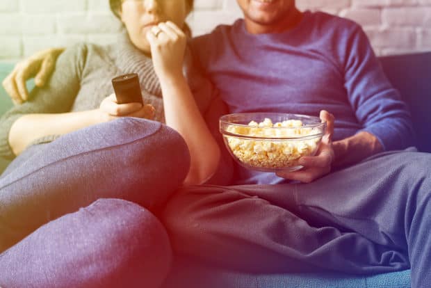 einPaar sitzt auf dem Sofa und isst poppcorn und trinkt bier