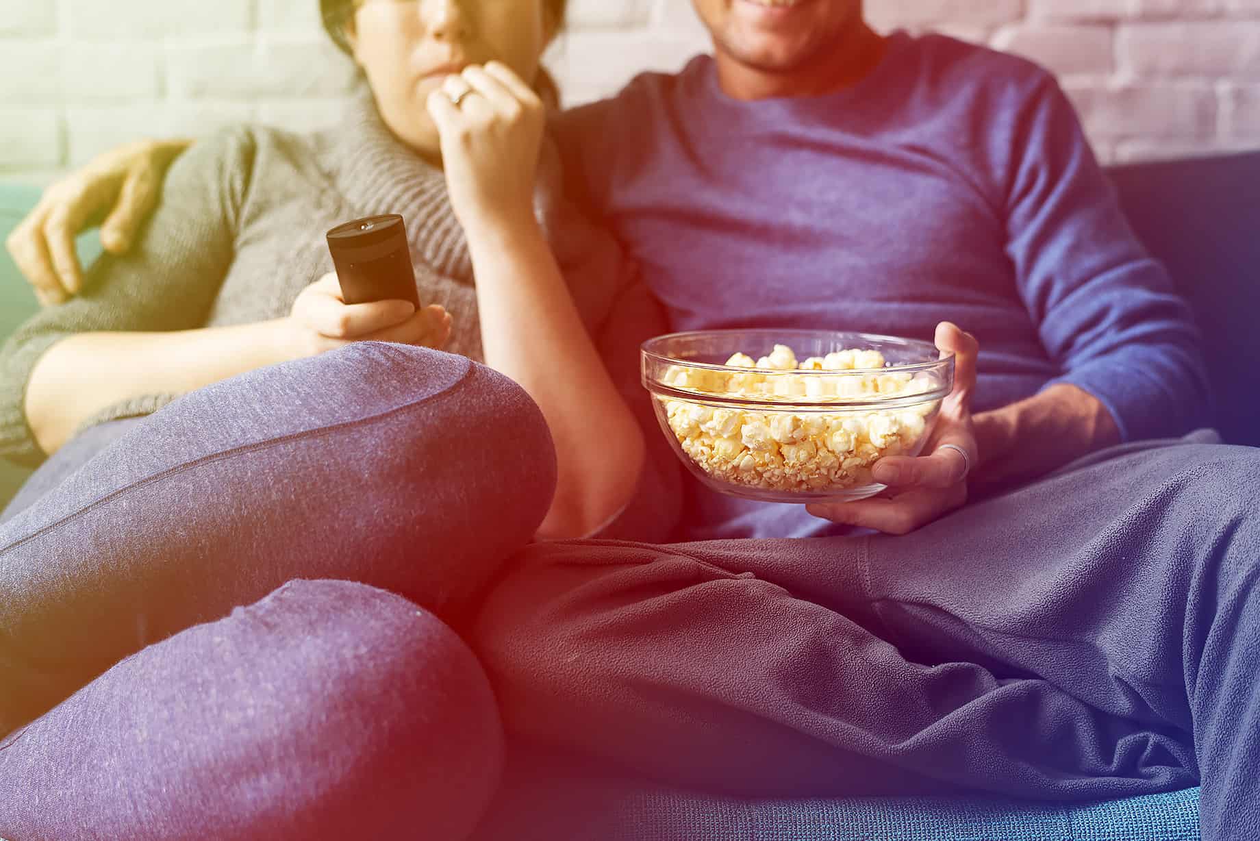 ein Paar sitzt auf dem Sofa und isst poppcorn und trinkt bier
