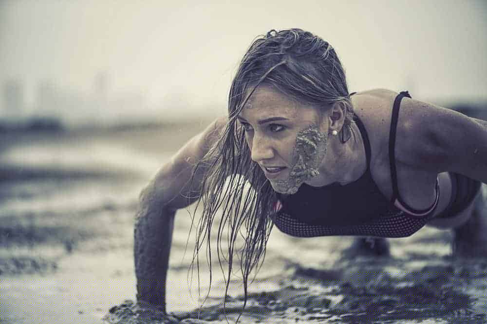 Trainierte Frau macht Crawling Fitness und krabbelt durch den Schlamm