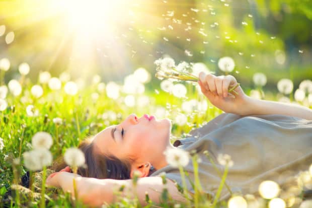 Junge Frau genießt den Moment liegt auf einer Wiese und pustet gegen eine Pusteblume.