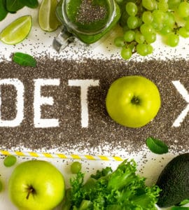 Tischplatte in der Mitte steht das Wort DETOX, darüber und darunter grünes Gemüse und Obst