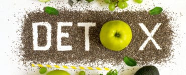 Tischplatte in der Mitte steht das Wort DETOX, darüber und darunter grünes Gemüse und Obst