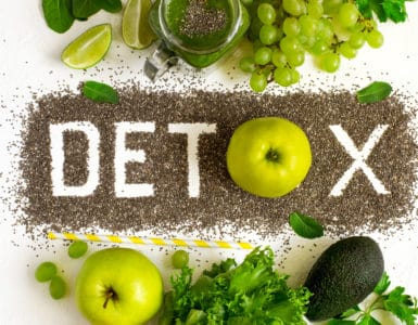 Tischplatte in der Mitte steht das Wort DETOX, darüber und darunter grünes Gemüse und Obst