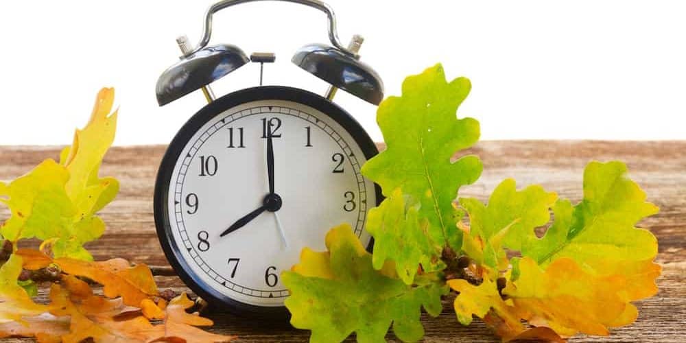 Wecker auf Holztisch mit buntem Herbstlaub