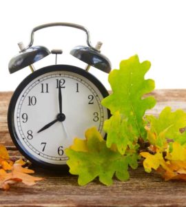 Wecker auf Holztisch mit buntem Herbstlaub