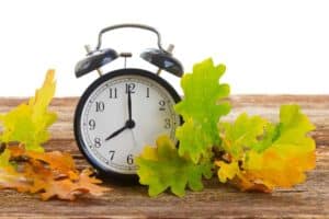 Wecker auf Holztisch mit buntem Herbstlaub