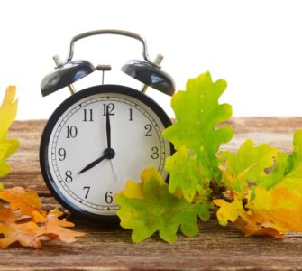 Wecker auf Holztisch mit buntem Herbstlaub
