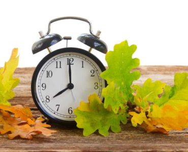 Wecker auf Holztisch mit buntem Herbstlaub