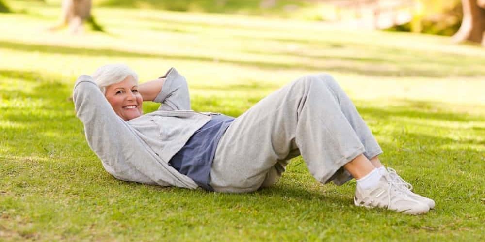 Bestager Fitness Ältere fitte Frau in Sportkleidung im Park liegt auf Wiese und macht Crunches